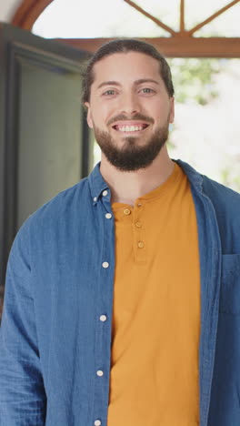 Vertical-video-of-happy-caucasian-man-with-beard-standing-and-smiling-in-sunny-house