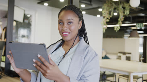 Portrait-of-happy-african-american-casual-businesswoman-using-tablet-standing-in-office,-slow-motion