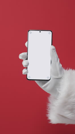 Vertical-video-of-santa-claus-holding-smartphone-with-copy-space-on-red-background