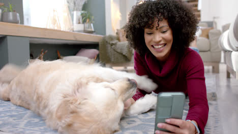 Feliz-Mujer-Birracial-Con-Perro-Golden-Retriever-Usando-Un-Teléfono-Inteligente-En-Casa,-Cámara-Lenta