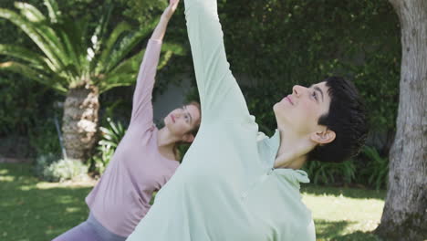 Happy-caucasian-lesbian-couple-practising-yoga-in-sunny-garden,-slow-motion
