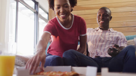 Video-Eines-Glücklichen-Afroamerikanischen-Paares,-Das-Auf-Dem-Sofa-Sitzt-Und-Pizza-Isst