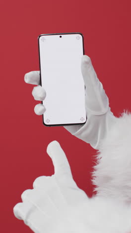 Vertical-video-of-santa-claus-holding-smartphone-with-copy-space-on-red-background