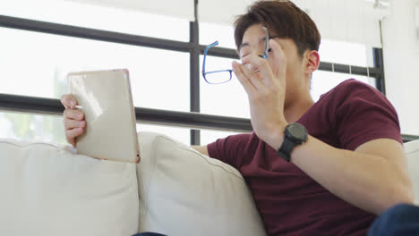 Asiatischer-Männlicher-Teenager-Trägt-Eine-Brille-Und-Benutzt-Ein-Tablet-Im-Wohnzimmer