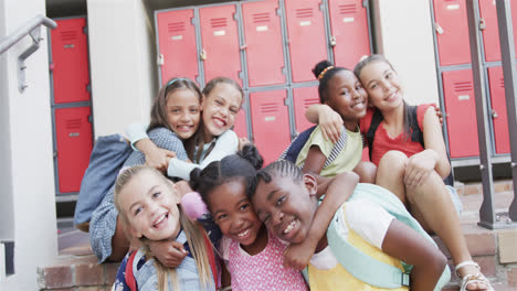 Portrait-of-happy-diverse-schoolgirls-embracing-each-other-at-school-lockers-at-elementary-school