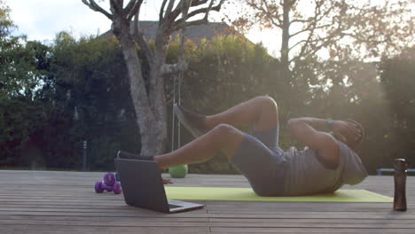 African-American-man-exercises-outdoors,-following-an-online-workout