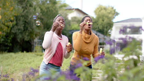 Glückliche-Afroamerikanische-Tochter-Und-Mutter-Pusten-Seifenblasen-Im-Sonnigen-Garten
