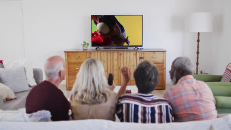 Senior-diverse-friends-watching-tv-with-diverse-male-rugby-players-playing-on-screen