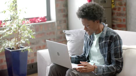 Happy-african-american-man-sitting-on-sofa-using-laptop-at-home,-slow-motion
