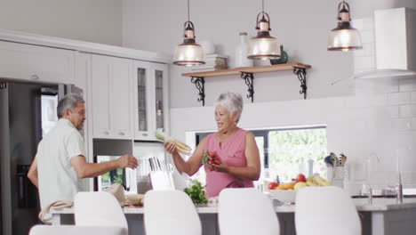 Happy-senior-biracial-couple-putting-vegetables-in-fridge-in-kitchen