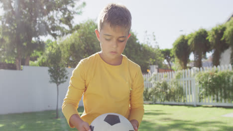Portrait-of-happy-caucasian-boy-holding-football-in-garden,-slow-motion