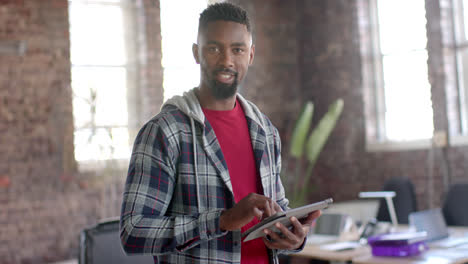 Portrait-of-happy-african-american-casual-businessman-using-tablet-in-office-in-slow-motion