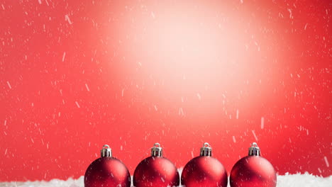 Animation-of-snow-falling-over-red-baubles-against-copyspace-on-red-gradient-background