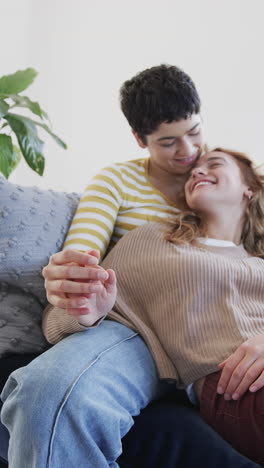 Happy-caucasian-lesbian-couple-lying-on-sofa-and-holding-hands-in-sunny-living-room