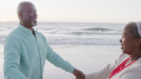 Happy-senior-african-american-couple-dancing-at-beach,-in-slow-motion