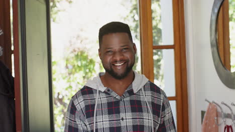 Happy-african-american-man-with-beard-standing-and-smiling-in-sunny-house