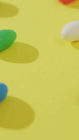 Video-of-close-up-of-rows-of-multi-coloured-sweets-over-yellow-background