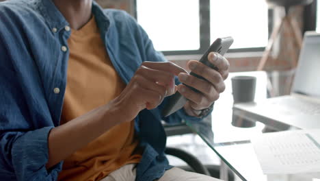 Midsection-of-african-american-casual-businessman-sitting-using-smartphone-at-home,-slow-motion