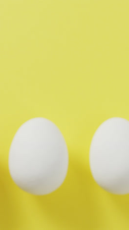 Video-of-row-of-one-brown-and-four-white-eggs-with-copy-space-on-yellow-background