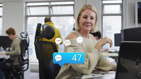 Animation-of-message-icons-floating-with-increasing-numbers-over-caucasian-woman-smiling-at-office