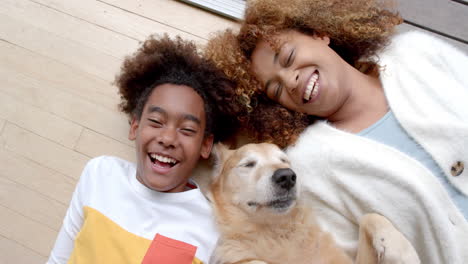 Portrait-of-happy-african-american-mother-and-son-lying-on-floor,-with-their-pet-dog,-slow-motion