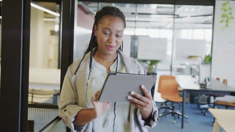 Happy-african-american-casual-businesswoman-using-tablet-standing-in-office,-in-slow-motion