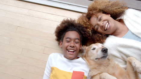 Portrait-of-happy-african-american-mother-and-son-lying-on-floor,-with-their-pet-dog,-slow-motion