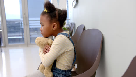 Sad-african-american-girl-sitting-in-hospital-waiting-room-and-holding-mascot,-slow-motion