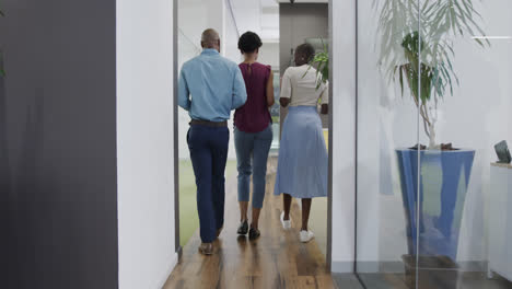 Rear-view-of-african-american-business-people-talking-and-walking-in-office-corridor,-in-slow-motion
