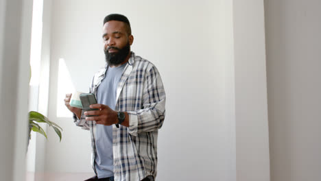 Hombre-Afroamericano-Tomando-Café-Y-Usando-Un-Teléfono-Inteligente-En-Casa,-Cámara-Lenta