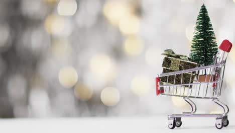 Video-of-shopping-trolley-with-christmas-tree-and-gifts-and-copy-space-on-fairy-lights-background