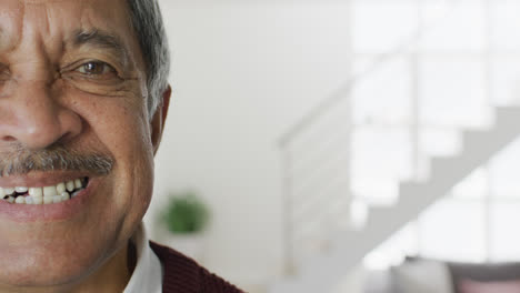 Video-close-up-portrait-of-senior-biracial-man-in-living-room-smiling-to-camera,-with-copy-space