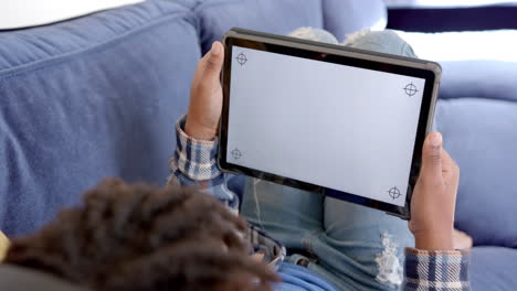 Afroamerikanischer-Junge,-Der-Ein-Tablet-Mit-Kopierplatz-Auf-Dem-Bildschirm-Benutzt-Und-Zu-Hause-Auf-Dem-Sofa-Liegt,-Zeitlupe