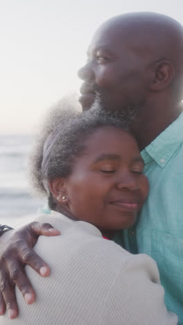 Vertical-video-of-senior-african-american-couple-embracing-at-beach,-in-slow-motion