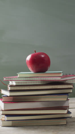 Vertikales-Video-Eines-Apfels-Auf-Einem-Stapel-Schulbücher-Auf-Dem-Schreibtisch-Mit-Einer-Kreidetafel-Im-Hintergrund