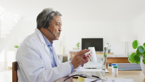 Senior-biracial-male-doctor-using-headset-and-laptop-for-video-consultation-call