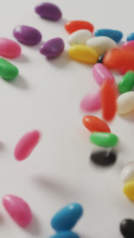 Video-of-close-up-of-multi-coloured-sweets-falling-over-white-background