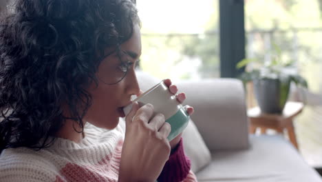 Biracial-woman-drinking-coffee-on-sofa-at-home,-slow-motion