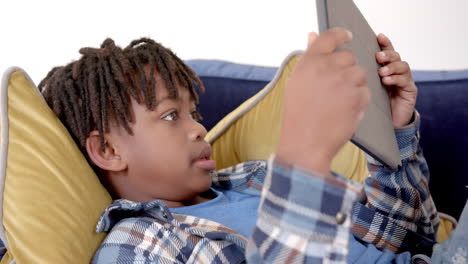 African-american-boy-using-tablet-lying-on-sofa-at-home,-slow-motion