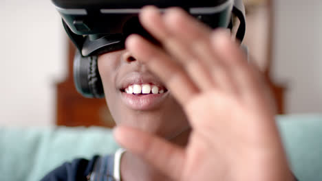 African-american-girl-using-vr-headset-and-touching-virtual-screen-in-living-room,-slow-motion