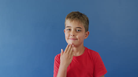 Portrait-of-happy-caucasian-boy-using-sign-language-on-blue-background,-slow-motion