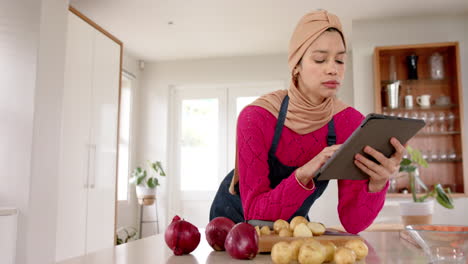 Biracial-Frau-Im-Hijab-Mit-Tablet,-Die-Zu-Hause-In-Der-Küche-Essen-Zubereitet,-Mit-Kopierraum,-Zeitlupe