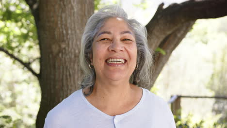 Portrait-of-happy-senior-biracial-woman-with-grey-hair-in-sunny-nature,-copy-space,-slow-motion