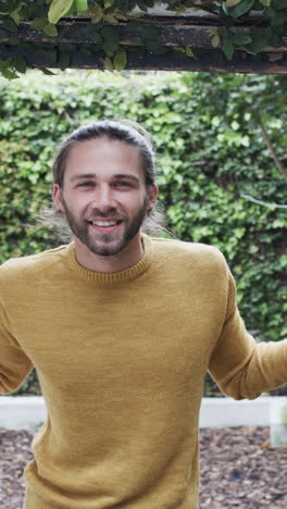 Vertical-video-of-portrait-of-happy-caucasian-man-wearing-yellow-jumper-in-garden,-slow-motion