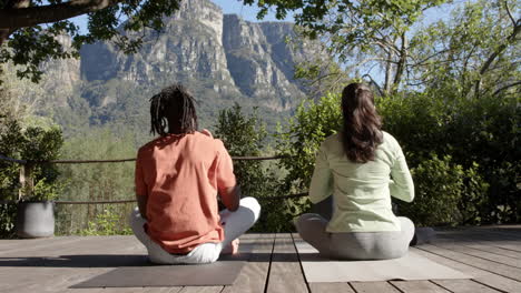 Rear-view-of-diverse-couple-practicing-yoga-meditation-sitting-in-sunny-nature,-slow-motion