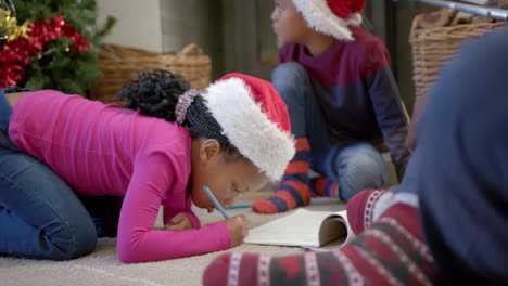 African-american-brother-and-sister-in-christmas-hats-drawing-on-floor-in-living-room,-slow-motion