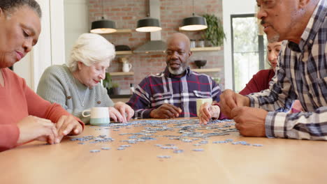 Happy-diverse-senior-female-and-male-friends-talking-and-doing-jigsaw-puzzle-in-kitchen,-slow-motion