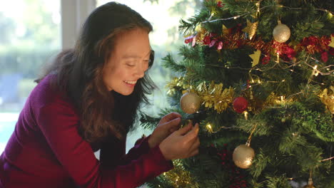 Happy-biracial-woman-decorating-christmas-tree-and-smiling,-slow-motion