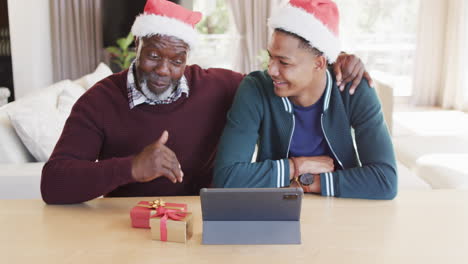 Feliz-Padre-Afroamericano-E-Hijo-Adulto-Con-Sombreros-De-Navidad-Con-Videollamada-De-Tableta,-Cámara-Lenta