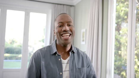 Porträt-Eines-Glücklichen-Afroamerikanischen-Mannes,-Der-Im-Sonnigen-Wohnzimmer-Steht-Und-Lächelt,-Zeitlupe